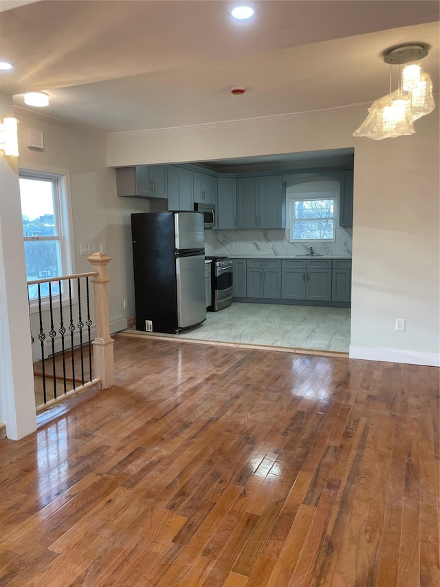 kitchen with appliances with stainless steel finishes, decorative backsplash, light hardwood / wood-style floors, hanging light fixtures, and ornamental molding