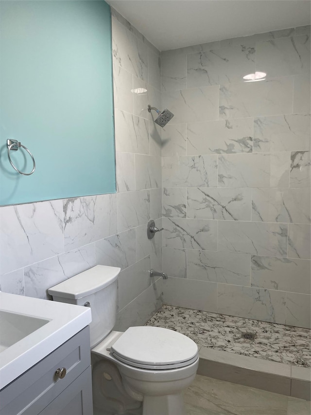 bathroom featuring tile walls, tiled shower, vanity, and toilet