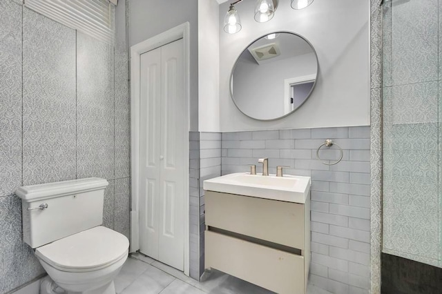 bathroom featuring tile patterned floors, vanity, toilet, and tile walls