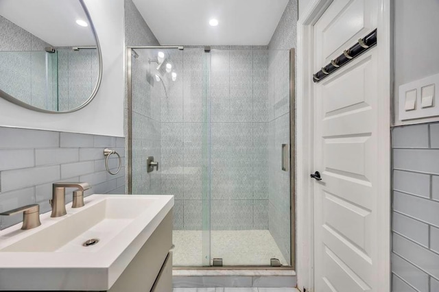 bathroom featuring backsplash, vanity, a shower with shower door, and tile walls