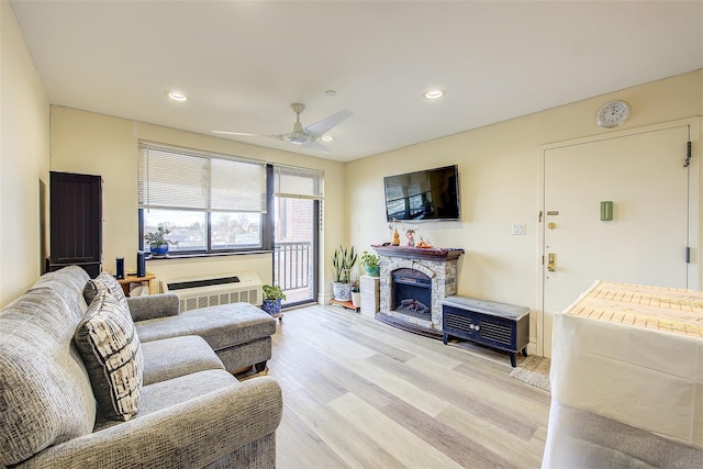 living room featuring a stone fireplace, ceiling fan, and light hardwood / wood-style flooring