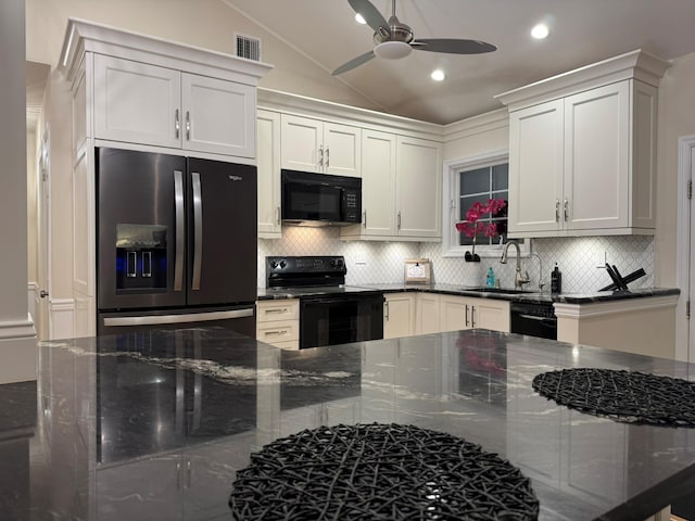 kitchen with dark stone counters, black appliances, white cabinets, sink, and vaulted ceiling