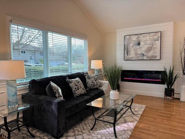 living room featuring a large fireplace, a baseboard radiator, wood-type flooring, and vaulted ceiling