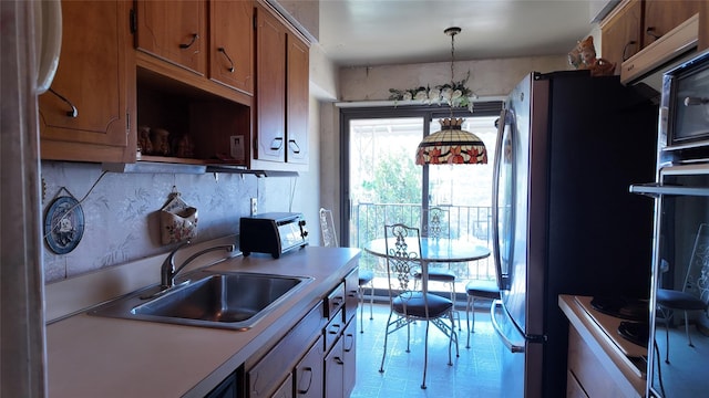 kitchen with light countertops, a sink, freestanding refrigerator, brown cabinets, and decorative backsplash