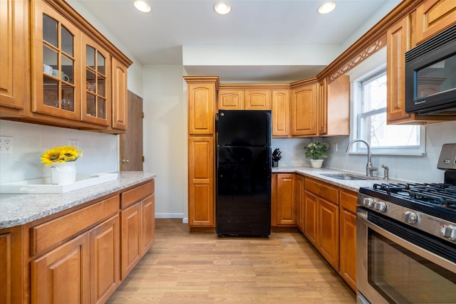 kitchen with backsplash, black appliances, sink, light hardwood / wood-style floors, and light stone counters