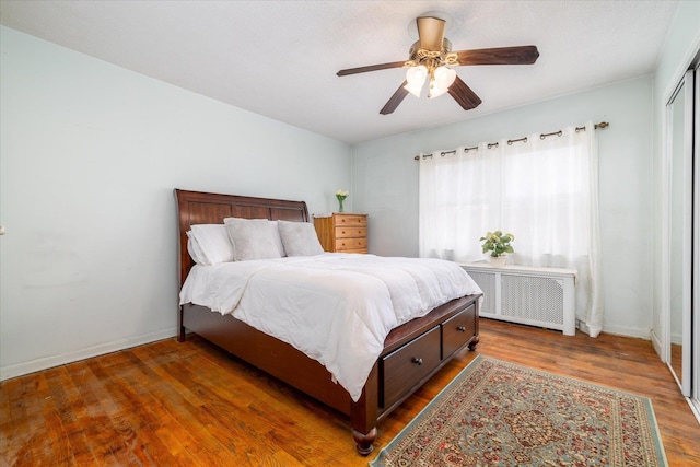 bedroom featuring ceiling fan, radiator heating unit, dark wood-type flooring, and a closet