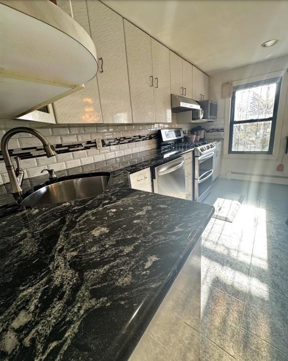 kitchen featuring sink, stainless steel appliances, tasteful backsplash, a baseboard heating unit, and dark stone countertops