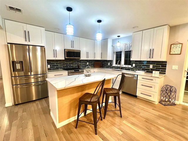 kitchen featuring pendant lighting, light hardwood / wood-style floors, a kitchen island, appliances with stainless steel finishes, and white cabinets