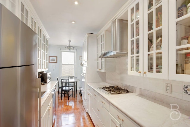 kitchen featuring backsplash, light stone counters, stainless steel appliances, wall chimney range hood, and white cabinetry