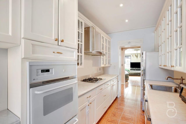 kitchen featuring stainless steel gas cooktop, sink, wall chimney range hood, oven, and white cabinetry