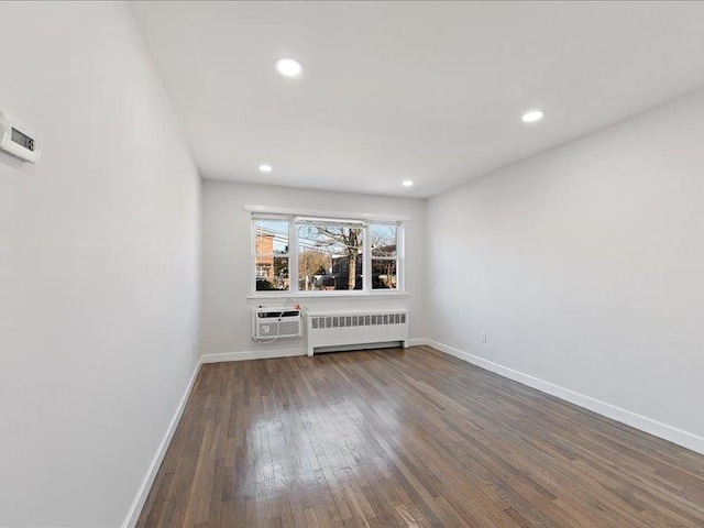 empty room featuring a wall mounted AC, hardwood / wood-style flooring, and radiator