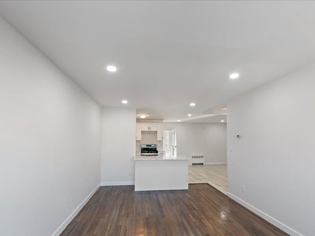 kitchen featuring radiator, stainless steel range oven, tasteful backsplash, dark hardwood / wood-style flooring, and white cabinetry