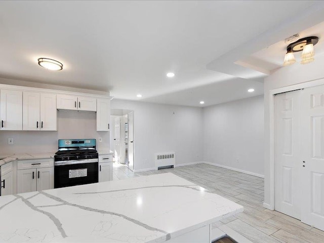 kitchen with radiator, black gas range oven, light stone counters, white cabinets, and light wood-type flooring