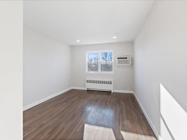 empty room featuring a wall mounted air conditioner, dark hardwood / wood-style floors, and radiator