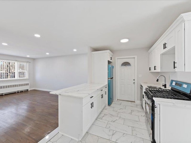 kitchen featuring light stone counters, gas stove, white cabinets, radiator heating unit, and stainless steel refrigerator