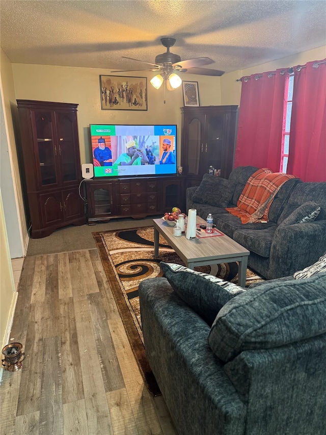 living room with ceiling fan, a textured ceiling, and light wood-type flooring