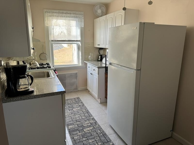 kitchen featuring sink, light tile patterned floors, white refrigerator, white cabinets, and backsplash