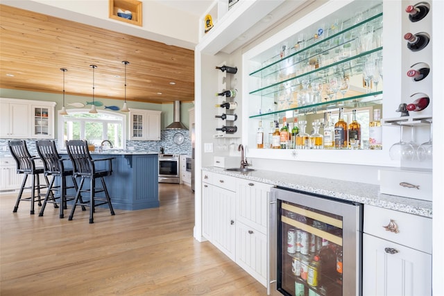 bar with white cabinets, light stone countertops, wood ceiling, and beverage cooler