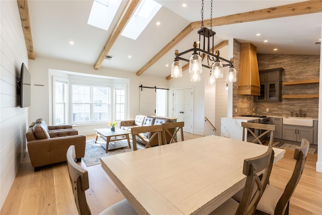 dining room featuring light wood-type flooring, a skylight, sink, a barn door, and beamed ceiling