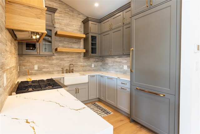 kitchen with sink, gray cabinets, paneled refrigerator, light wood-type flooring, and light stone counters