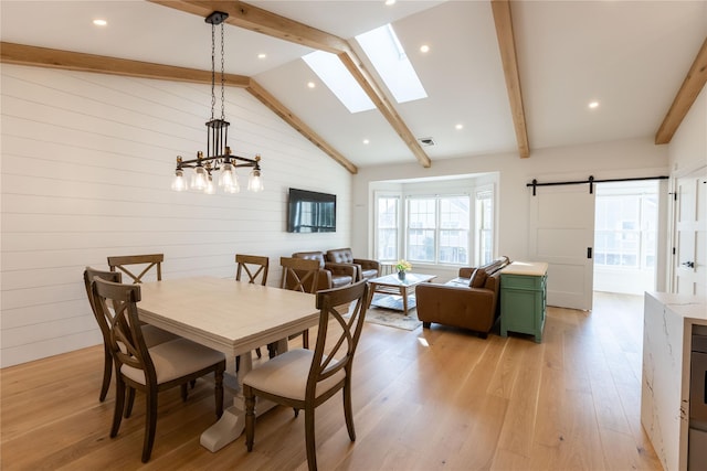 dining room featuring a barn door, a skylight, light hardwood / wood-style flooring, and wooden walls