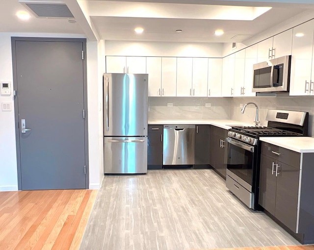 kitchen with sink, tasteful backsplash, light hardwood / wood-style floors, white cabinetry, and stainless steel appliances