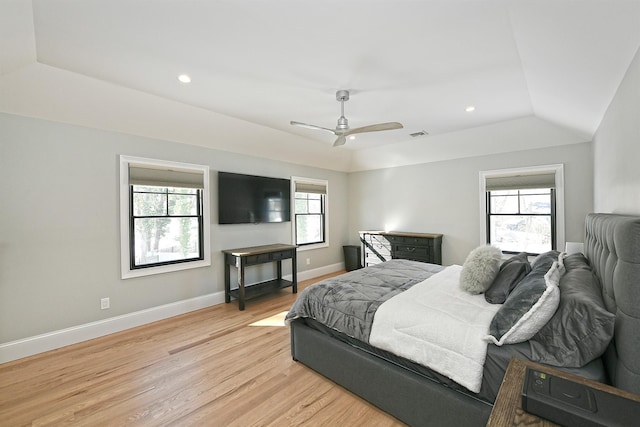 bedroom with ceiling fan, lofted ceiling, a tray ceiling, and light hardwood / wood-style flooring