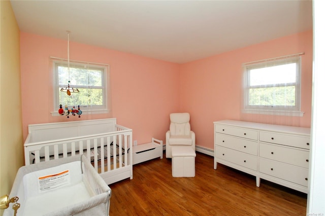 bedroom featuring dark hardwood / wood-style floors, a baseboard heating unit, and a nursery area