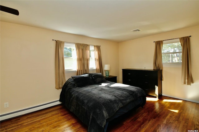 bedroom with a baseboard radiator, multiple windows, and dark wood-type flooring