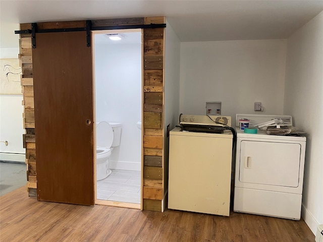 clothes washing area featuring a barn door, separate washer and dryer, hardwood / wood-style floors, and a baseboard radiator