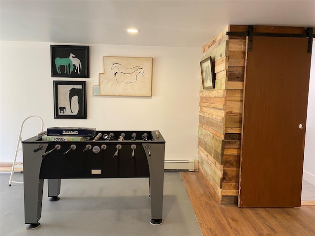 rec room with a barn door, light hardwood / wood-style floors, and a baseboard heating unit