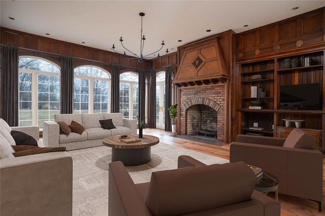 living room with a chandelier, hardwood / wood-style flooring, a brick fireplace, and wooden walls