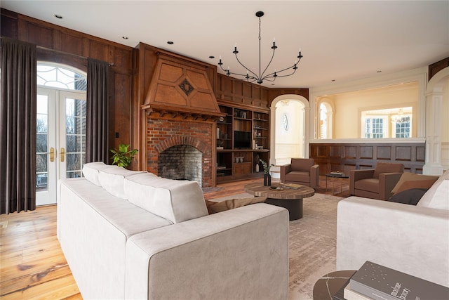 living room with a chandelier, french doors, light hardwood / wood-style floors, and wooden walls