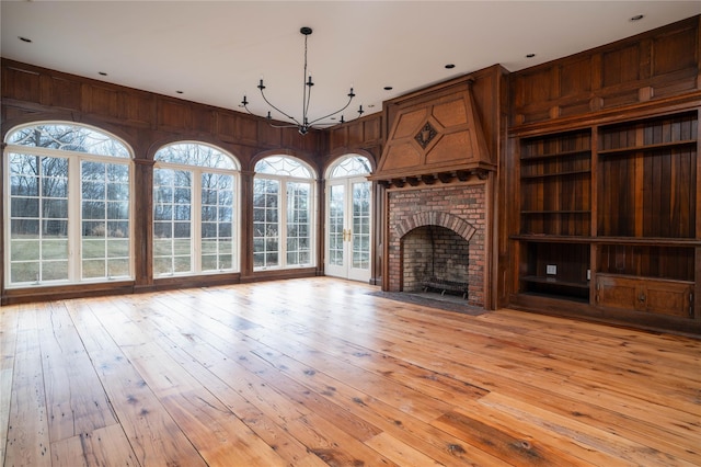 unfurnished living room featuring a notable chandelier, wood walls, a fireplace, and light hardwood / wood-style flooring