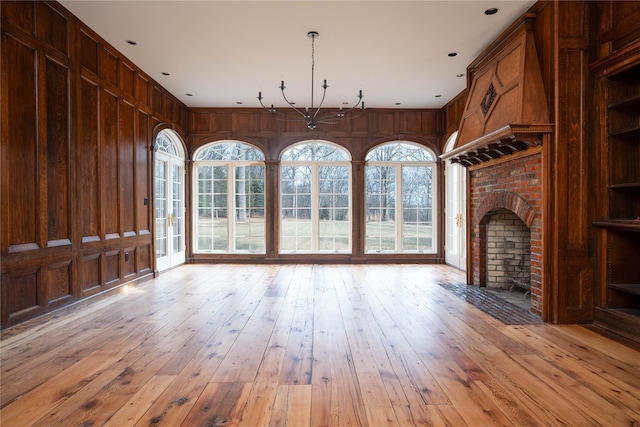 unfurnished living room featuring wood walls, light hardwood / wood-style floors, an inviting chandelier, and a brick fireplace