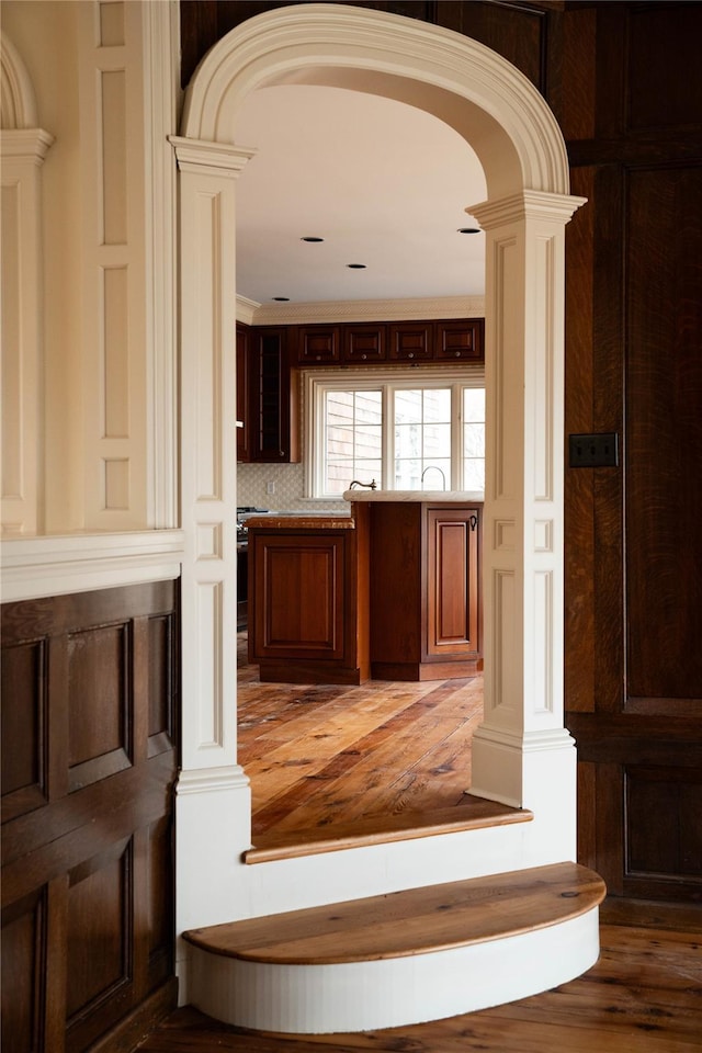 bar featuring tasteful backsplash, crown molding, decorative columns, and wood-type flooring