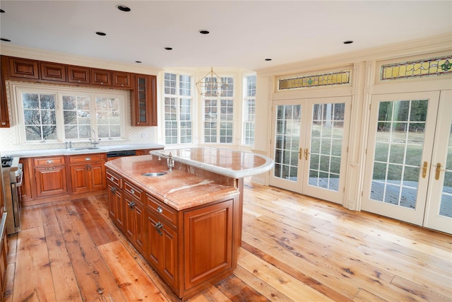 kitchen with french doors, gas range, crown molding, a center island with sink, and light hardwood / wood-style floors