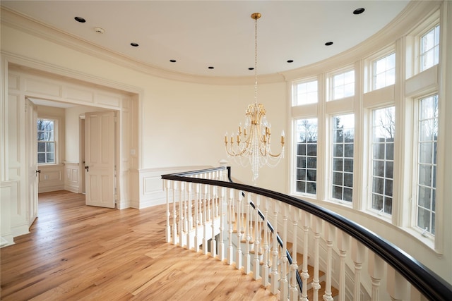 corridor featuring light hardwood / wood-style floors, an inviting chandelier, a wealth of natural light, and crown molding