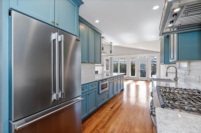 kitchen with blue cabinetry, stainless steel appliances, light hardwood / wood-style flooring, sink, and light stone counters