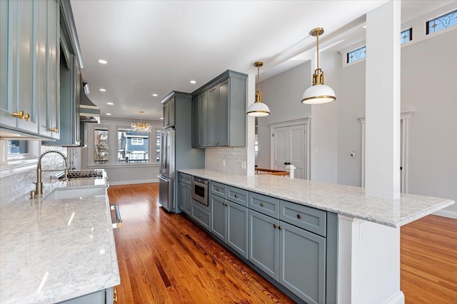 kitchen featuring kitchen peninsula, light stone countertops, appliances with stainless steel finishes, dark hardwood / wood-style floors, and pendant lighting