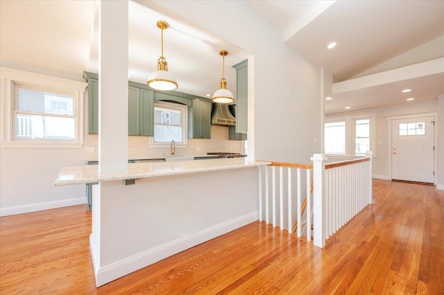 kitchen with light wood-type flooring, kitchen peninsula, green cabinets, decorative light fixtures, and custom range hood