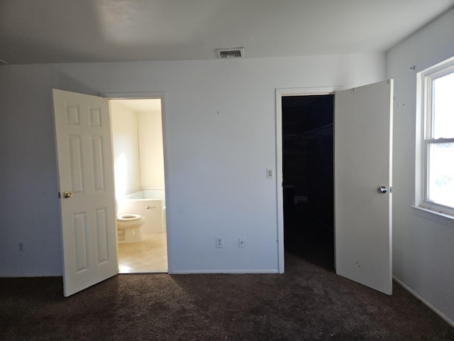 unfurnished bedroom with dark carpet, ensuite bathroom, a closet, and a walk in closet