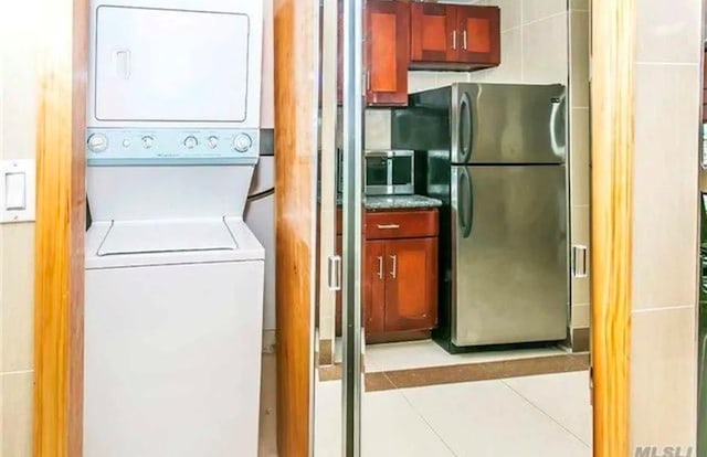 laundry room with light tile patterned floors and stacked washer / dryer