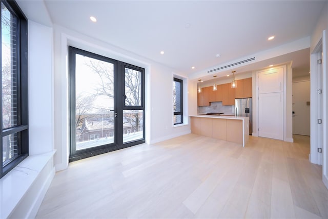 kitchen with light wood-type flooring, stainless steel fridge, backsplash, and pendant lighting