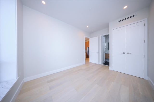 unfurnished bedroom with light wood-type flooring, ensuite bath, and stainless steel refrigerator