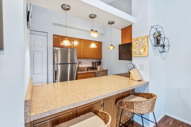 kitchen with backsplash, a kitchen breakfast bar, hanging light fixtures, appliances with stainless steel finishes, and kitchen peninsula