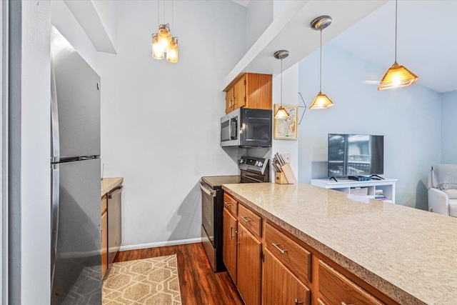 kitchen with kitchen peninsula, dark wood-type flooring, stainless steel appliances, and decorative light fixtures