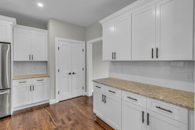 kitchen with backsplash, white cabinets, dark hardwood / wood-style floors, light stone countertops, and stainless steel refrigerator