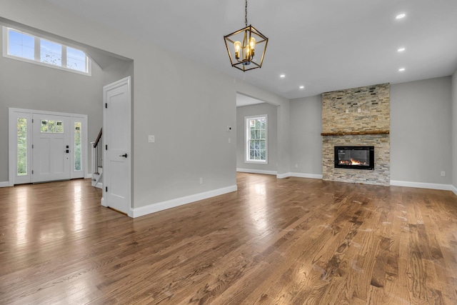 unfurnished living room featuring hardwood / wood-style flooring, a stone fireplace, and an inviting chandelier