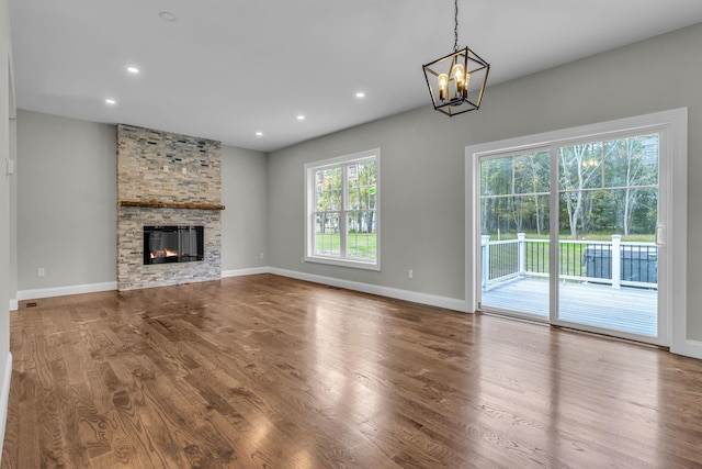 unfurnished living room with an inviting chandelier, hardwood / wood-style flooring, and a stone fireplace